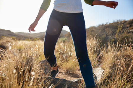 Girls legs wearing jeggings and a white t-shirt climbing over rocks on a grassy hill in bright...