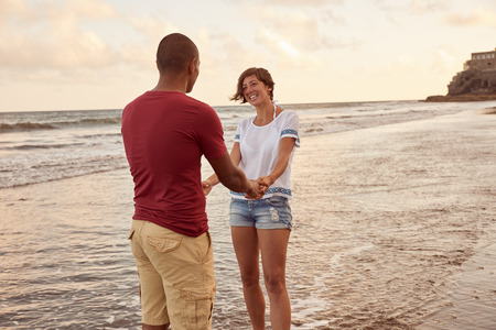 Happy couple with a profoundly deep love for each other looking at each other while standing in the breaking waves on the beachの写真素材