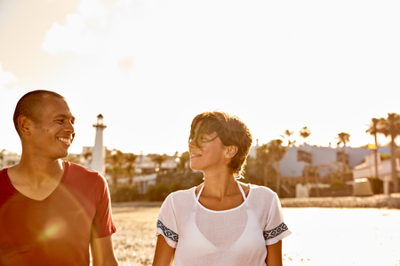 Loving couple with eyes for only each other holding hands while enjoying a lovely walk on the empty beach with bright white sky behind themの写真素材