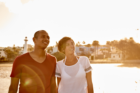 Intimate couple holding hands while looking up at the sky on the beach with a clear white sky and reflection behind themの写真素材
