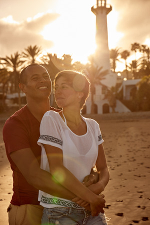Embracing adult couple in front of a lighthouse in a loving embrace enjoying the sun setting behind the lighthouseの写真素材