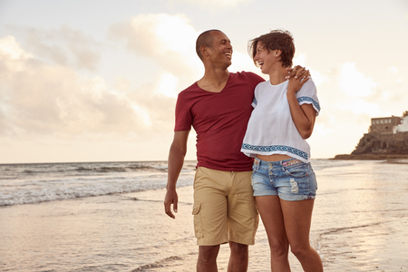 Joyfully laughing embracing couple in love looking at each other on the beach front while walking in the waves breaking around their feetの写真素材