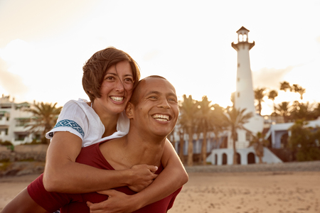 Loving couple in love piggy back riding on the beach while enjoying the last rays of the sun as it sets behind themの写真素材