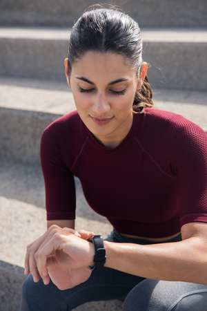 Beautiful brunette on stairs looking at watch or fitness trackerの写真素材