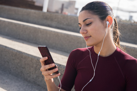 Young female brunette on stairs with cell phone and head set with hair pulled back