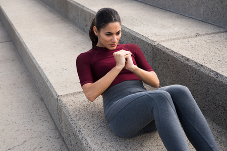Pretty young brunette doing stomach crunches in maroon top and grey thights with hair tied backの写真素材