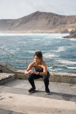 Sporty young woman exercising at the beach in a crouching position on some stairsの写真素材