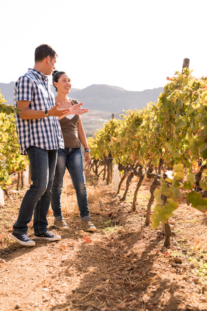 Man and a woman standing in the winelands wearing blue jeans and casual tops and talking to each otherの写真素材
