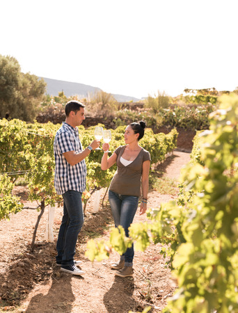Woman and man standing in the vineyards in casual clothing enjoying a glass of wineの写真素材