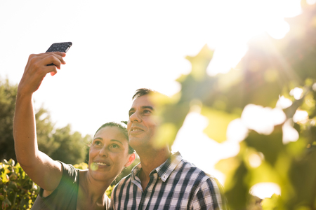 Handome man and woman taking a selfie with a phone in the vineyards on a sunny dayの写真素材