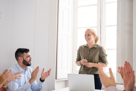 Woman smiling as fellow colleagues clap as she has completed her presentation to them in a sunlight office with a large windowの写真素材