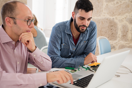 Bearded tech gay and a balding man are in front of a lap top workingの写真素材