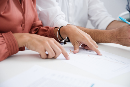 Woman sitting at a desk pointing at a document she is reading from as she sits next to a man in a white shirtの写真素材