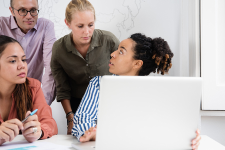 Business team in a meeting standing around a laptop talking to each other and looking at a laptop screenの写真素材