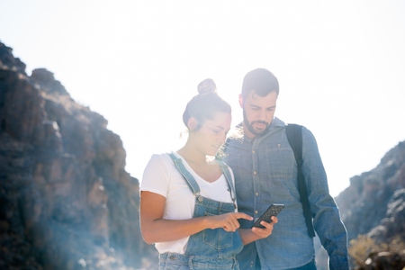 Couple standing in the mountains and looking down at a cell phone and pointing at the screenの写真素材