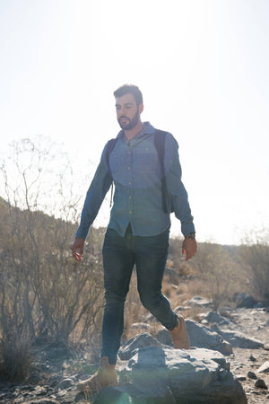 Man walking over rocks next to tall grass on a rocky path in the desertの写真素材