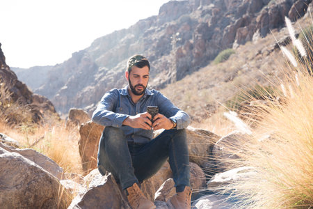 Close up of a man sitting on a rock in the mountains texting on a cell phoneの写真素材