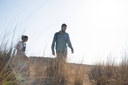 Man and woman walking in long grass with the mountains in the background