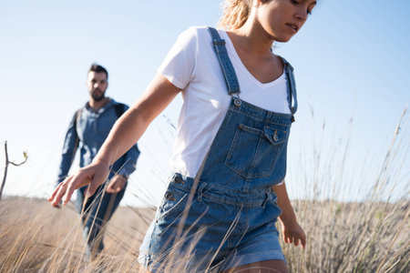Woman running through long grass with her arms open wide and a man follows herの写真素材