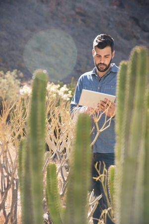 Man standing next to tall brown grass and a mountain using a pc tabletの写真素材
