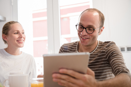 Couple sitting at a table looking at a pc tablet as he holds a glass of orange juice and they are both laughingの写真素材