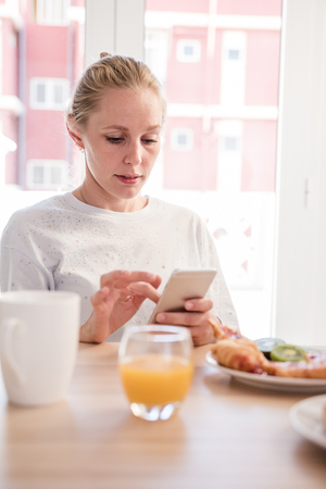 Woman sitting at a breakfast table looking down and texting from her cell phone, there is food on the tableの写真素材