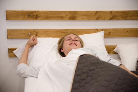 Woman lying in bed on her back and stretching with her eyes closedの写真素材