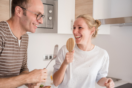 Couple dancing and singing in the kitchen as they stand together and laughの写真素材