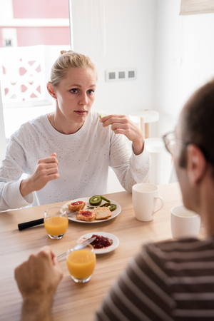 Couple sitting at a table in a kitchen having a breakfast and looking at each other from across the tableの写真素材