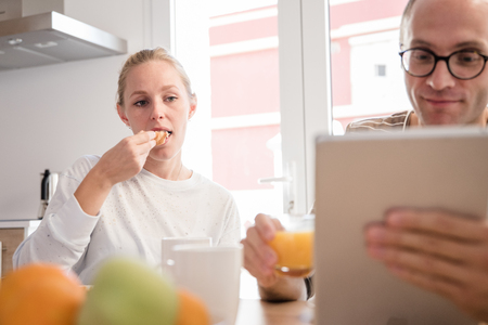 Couple sitting at a table looking at a pc tablet as he holds a glass of orange juice and she is eatingの写真素材