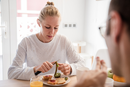 Close up of a woman sitting at a table looking down as she peels a piece of fruit at breakfastの写真素材