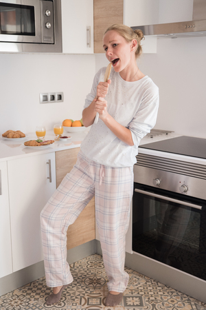 Woman dancing and singing in her kitchen, as she holds a kitchen utensil and pretends its a microphoneの写真素材