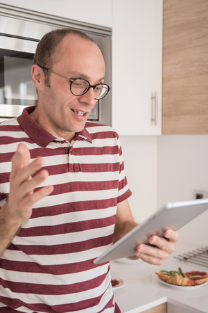 Man with a stripped shirt and glasses is holding a pc tables and gestures with his hand up while chattingの写真素材