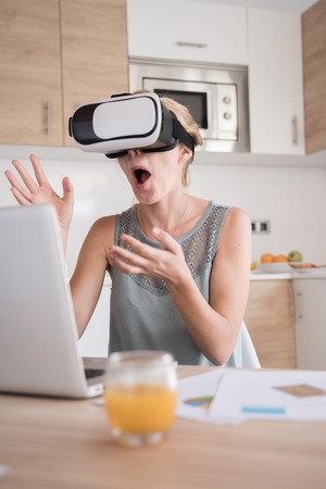Woman is gasping and laughing, her hands are in the air in front of her as she is wearing virtual reality glassesの写真素材