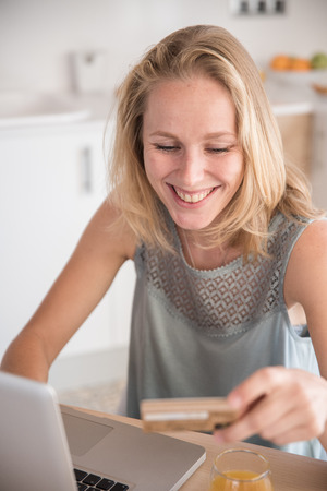 Woman smiling down at her credit cards that she is holding as she sits in front of a laptopの写真素材