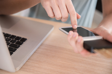 Woman texting on a cell phone that has a credit card device attached to it as she sits at a tableの写真素材