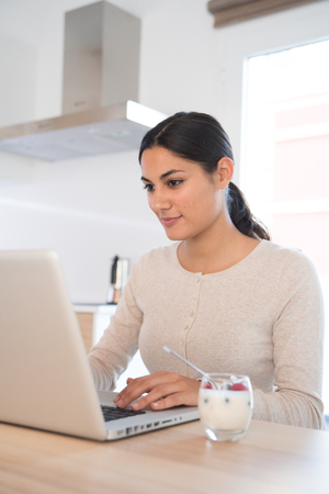 Woman sitting at a table in front of a a laptop pc , she is looking at the screen and typingの写真素材