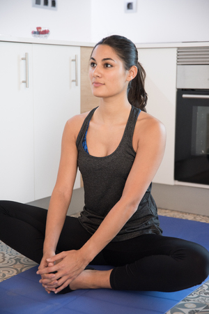 Woman looking straight ahead as she sits in a cross legged yoga pose on a blue matの写真素材