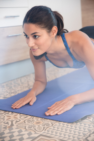 Woman doing a push up on a blue mat, her hands are flat on the floor and her head is upの写真素材