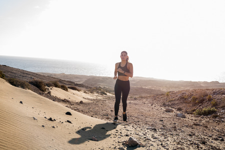 Long distance shot of a woman running across a rocky sand dune in the desertの写真素材