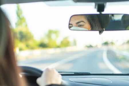 Woman wearing protective face mask while driving car. Reflection in rearview mirror. Protection...