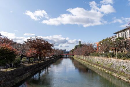 River view surrounded by some red leaves trees and with a but cloudy sky.