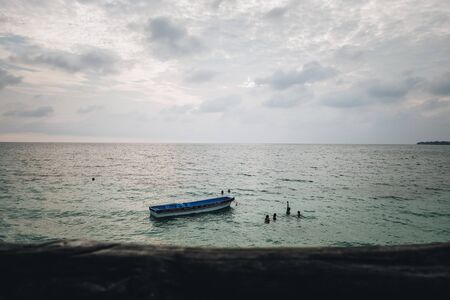 Children swimming around a boat on the beachの写真素材