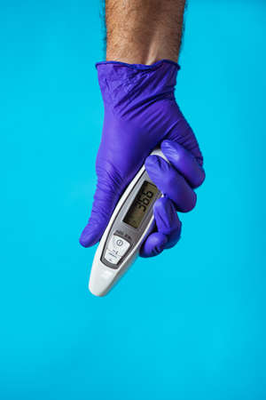 A doctor's hand wearing a purple glove holding a thermometer on blue background.の写真素材