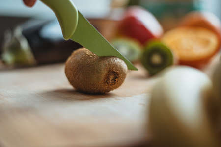 A kiwifruit being cut on a wooden table surrounded by other fruits.の写真素材