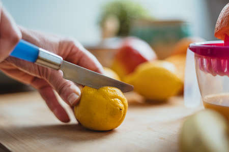 A woman cutting a lemon with a blue knife on a wooden table surrounded by other fruits.の写真素材