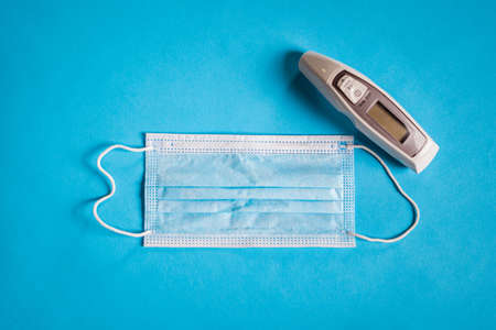 Medical face mask and thermometer on blue background.の写真素材