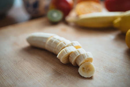 A chopped banana on a wooden table surrounded by other fruits.の写真素材
