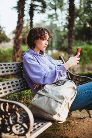 Girl sitting on a bench in a park looking at her mobile phone.の写真素材