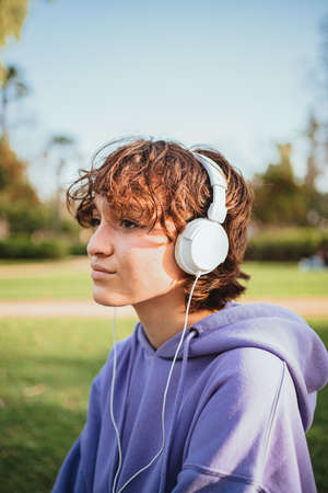 Relaxed teenager wearing white headphones listening to music in the park.の写真素材
